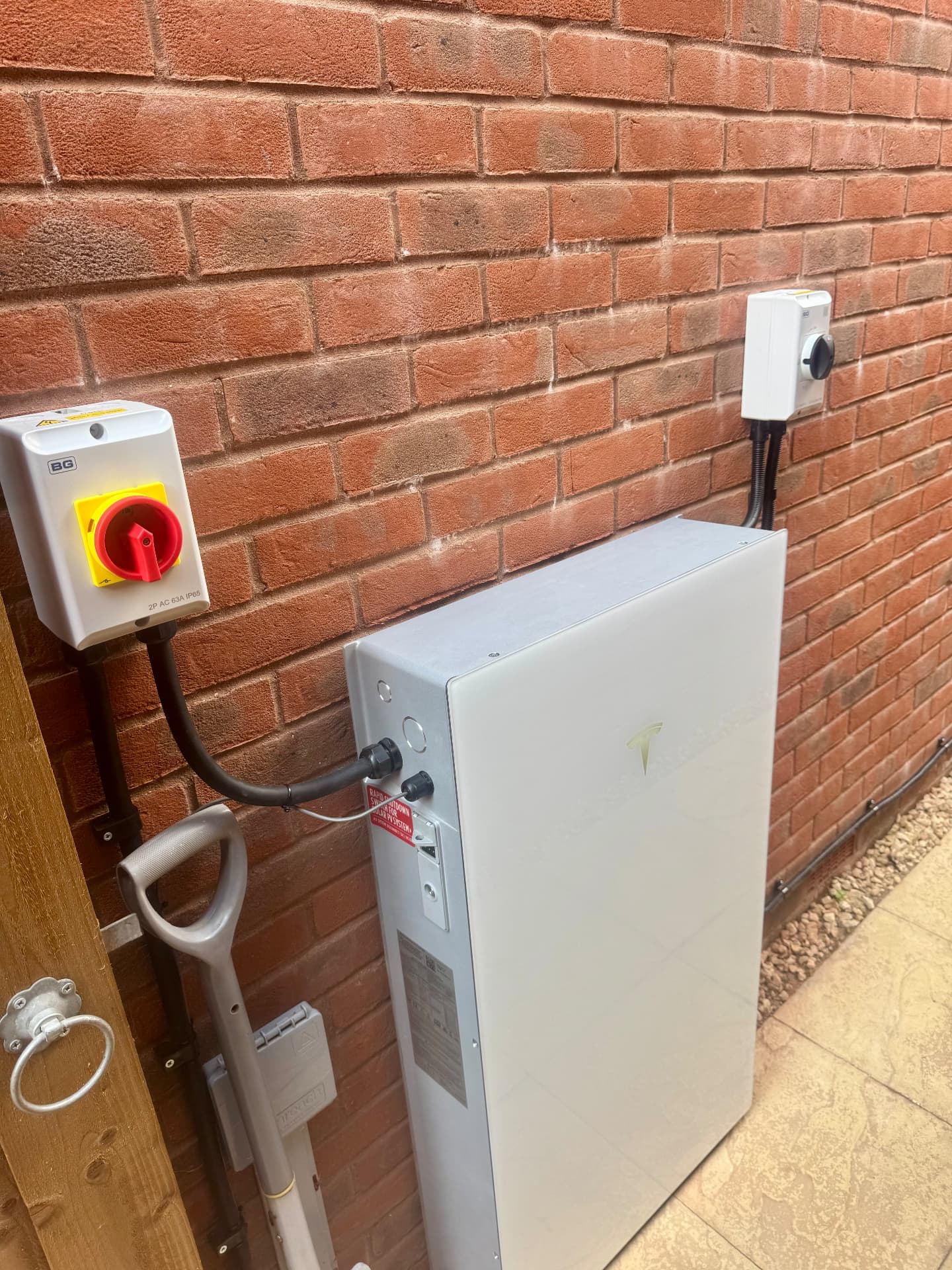 Outdoor Tesla home battery on a brick wall with electrical isolators and cabling
